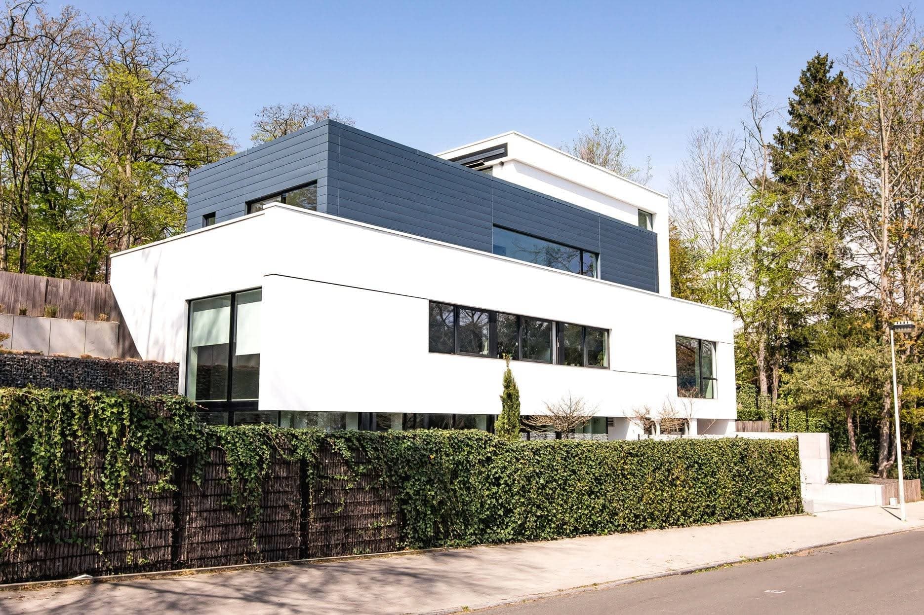Maison réalisée par COREMI : volume supérieur bardé anthracite sur socle enduit blanc, châssis noirs.