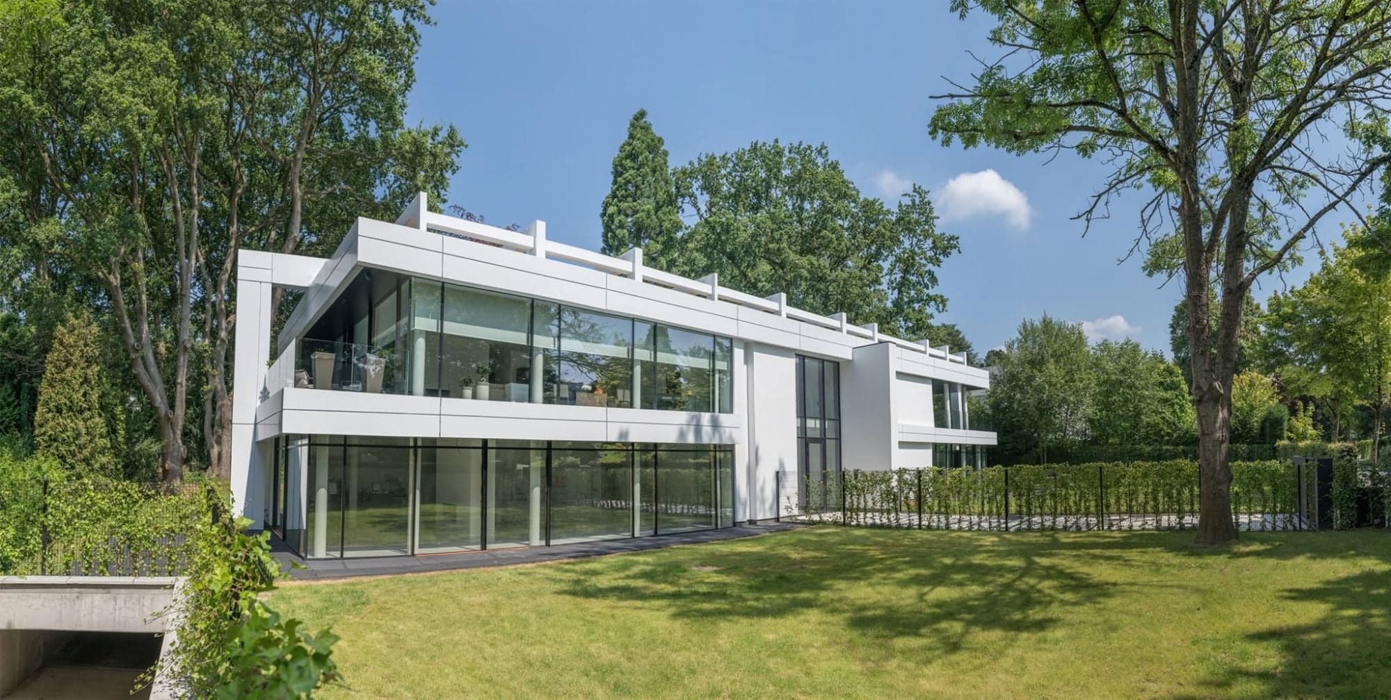 Villa contemporaine réalisée par COREMI : deux niveaux vitrés toute hauteur sous une pergola de toiture, jardin au premier plan.